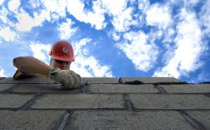 Photographie en contre-plongée d'un maçon travaillant sur un mur.