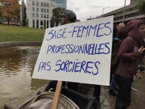 Photographie lors de la manifestation : une pancarte où il est écrit "Sage-femmes professionnelles, pas sorcières".