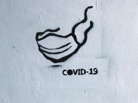 Photographie d'un graffiti représentant un masque. Il est écrit COVID-19 en dessous.