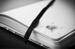 Photographie en noir et blanc d'un carnet ouvert où un coeur est dessiné sur le coin du bas d'une page.