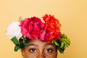 Portrait d'une personne noire avec des fleurs sur le dessus de la tête. Le portrait est coupé sous le nez.
