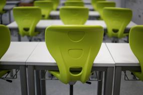 Photographie de tables blanches et de chaises vertes d'une salle de classe.
