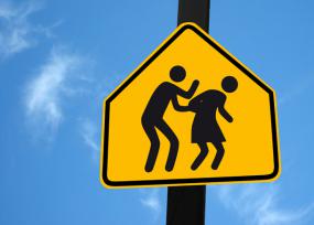 Détournement du panneau écoliers où le pictogramme représentant l'homme agresse le pictogramme représentant la femme.