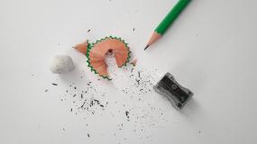 Photographie d'un crayon posé à côté d'un aiguisoir et de retailles de crayon.
