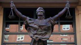 Photographie d'une statue de la justice qui se trouve devant des fenêtres.