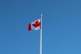 Photographie d'un mât avec le drapeau du Canada sur un ciel bleu.