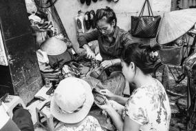 Photographie en noir et blancs de personnes qui travaillent  à réparer des chaussures dans un atelier exigu.