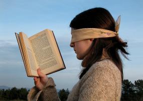 Une personne qui a les yeux bandées tient un livre devant ses yeux.