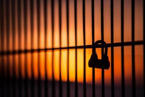 Photographie sur fond de soleil couchant d'un cadenas barré sur une clôture.