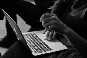 Photographie en noir et blanc ett en gros plan d'une personne travaillant sur un ordinateur portable posé sur ses genoux.
