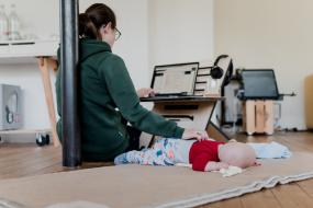 Vue biais d'une personne assise par terre travaillant à l'ordinateur. Un bébé est allongé à ses côtés.