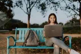 Une personne est assise sur un banc de parc avec son ordineur portable sur les genoux.