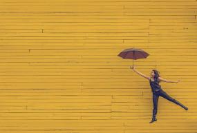 Sur un mur jaune, une personne semble s'envoler avec un parapluie.