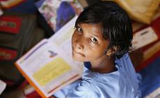 Un enfant assis par terre avec un livre, regard l'objectif de la caméra.