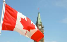 Photographie de la tour du parlement avec le drapeau canadien flottant en avant-plan.