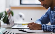 Une personne prend des notes en travaillant à l'ordinateur.