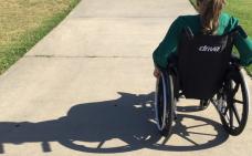 Photographie de dos d'une femme en fauteuil roulant.