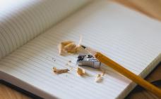 Sur un cahier ouvert, un crayon y est déposé à coté d'un aiguise crayon et de retailles de crayons.
