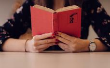 Photographie en gros plan sur le livre qu'une personne lit. La personne qui tient le livre a les bras posés sur une table.