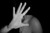 Photographie en noir et blanc d'une personne dont la main levée cache le visage.
