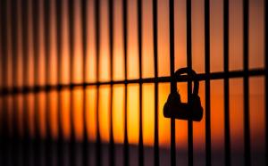 Photographie sur fond de soleil couchant d'un cadenas barré sur une clôture.
