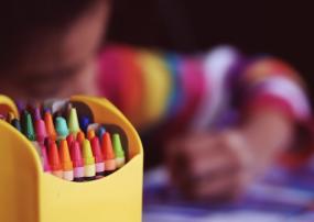 Photographie floutée d'un enfant qui semble colorier, avec une boîte de crayons en avant-plan.