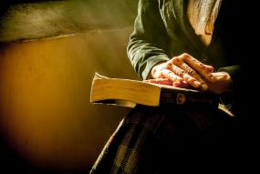 Photographie en gros plan sur les mains d'une personne âgée qui reposent sur un livre sur ses genoux.