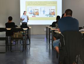 Photographie d'une salle de classe où un professeur se trouve à l'avant à côté d'une projection au mur.