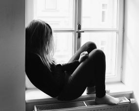 Photographie en noir et blanc d'une personne assise sur le rebord d'une fenêtre.