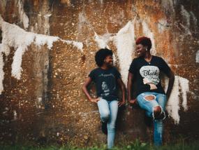 Photographie de deux personnes adossées à un mur. Elles se regardent et se sourient.