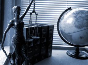 Sur un bureau, une statue de la justice, quatre livres et un globe terrestre.