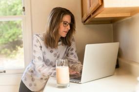 Une femme consulte son ordinateur portable sur le comptoir d'une cuisine.