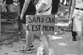 Photographie en noir et blanc d'une personne tenant une pancarte dans une manifestation où il est écrit "Sans oui, c'est non.
