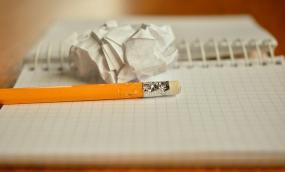 Photographie d'un cahier ouvert où sont déposés un crayon et une boulette de papier.