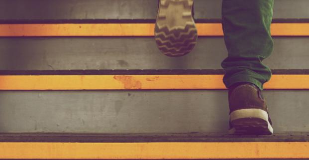 Photographie en gros plan sur les pieds d'une personne qui monte un escalier.